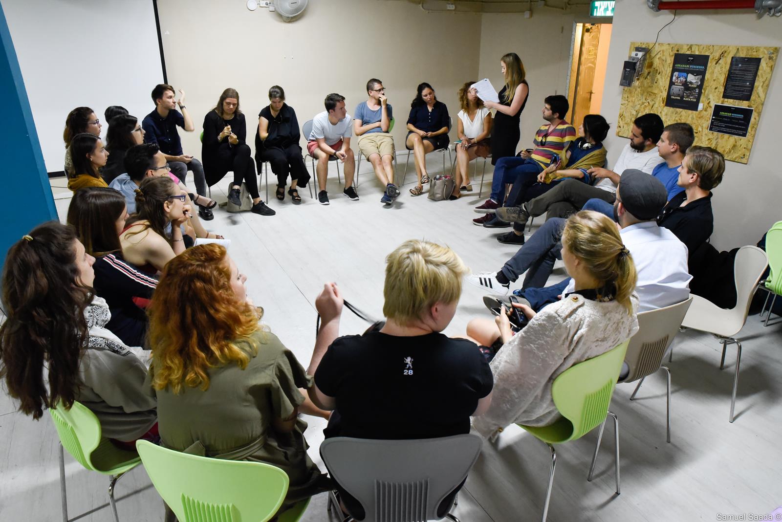 Uczestnicy programu znajdują się w sali, siedzą na krzesłach ustawionych w okrąg. Trwa podsumowanie programu w Izraelu.