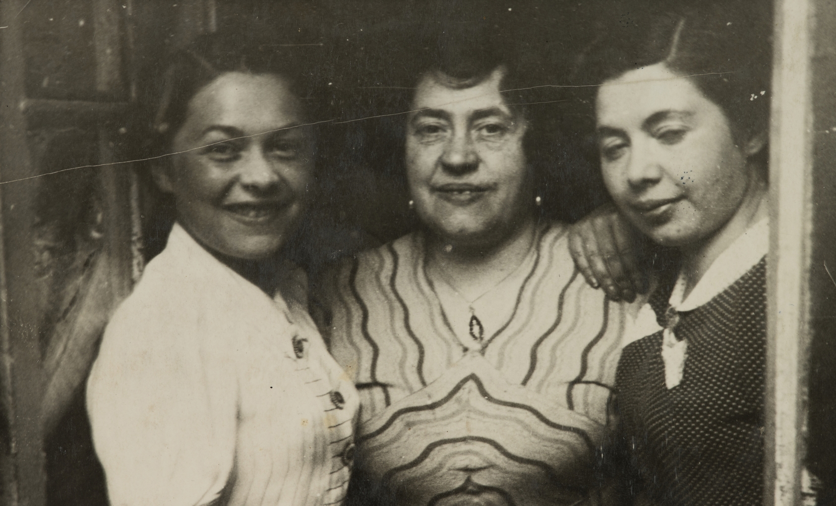 Fotografia z archiwum Muzeum POLIN. Przedstawia trzy kobiety, które pozują przytulone do siebie. Od lewej: Miriam Justman, Regina Justman, Paulina Włodawer