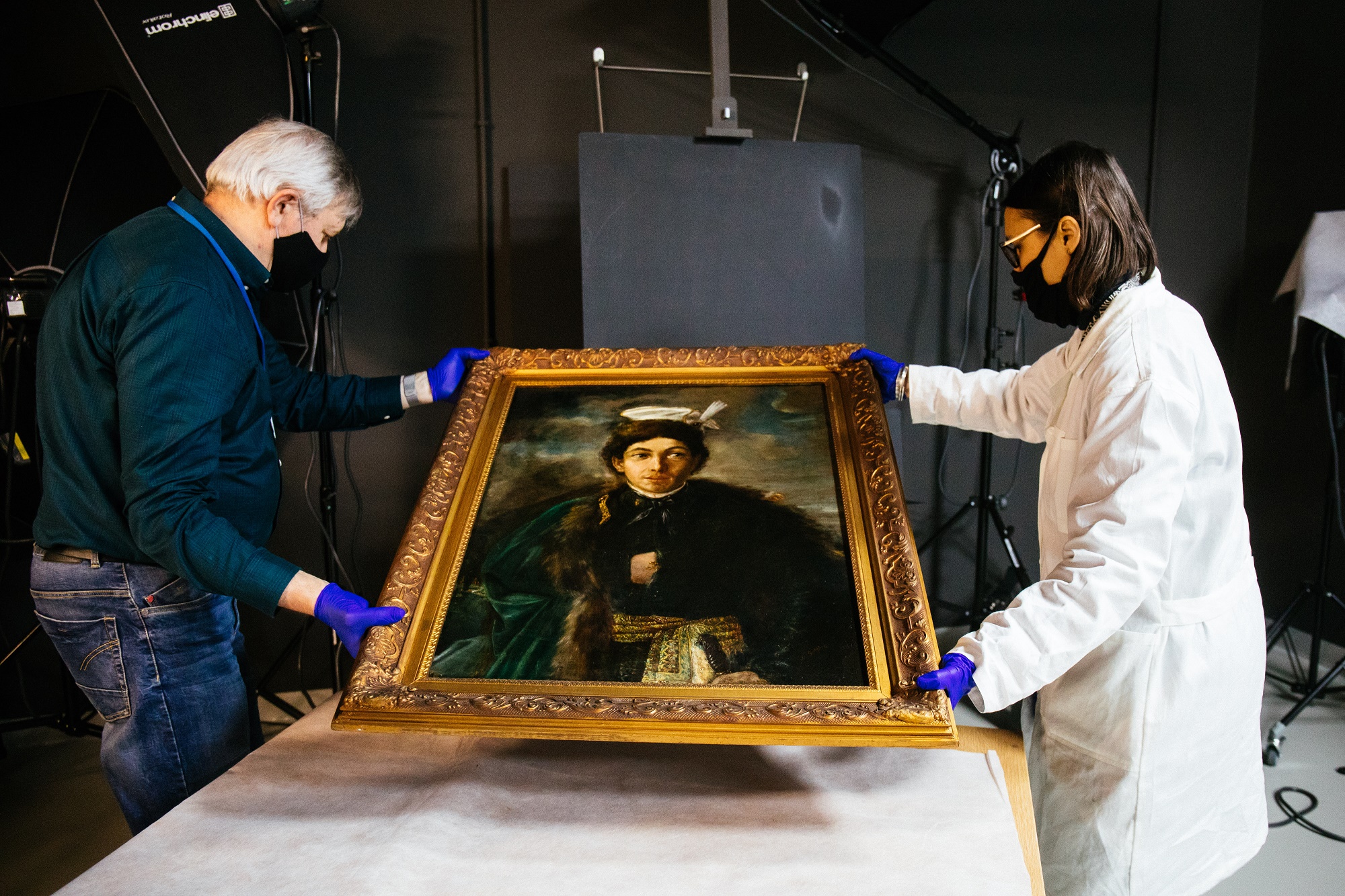 Na obrazie widzimy dwie osoby - kobietę i mężczyznę trzymających obraz Maurycy Gottlieb - „Autoportret w stroju polskiego szlachcica”