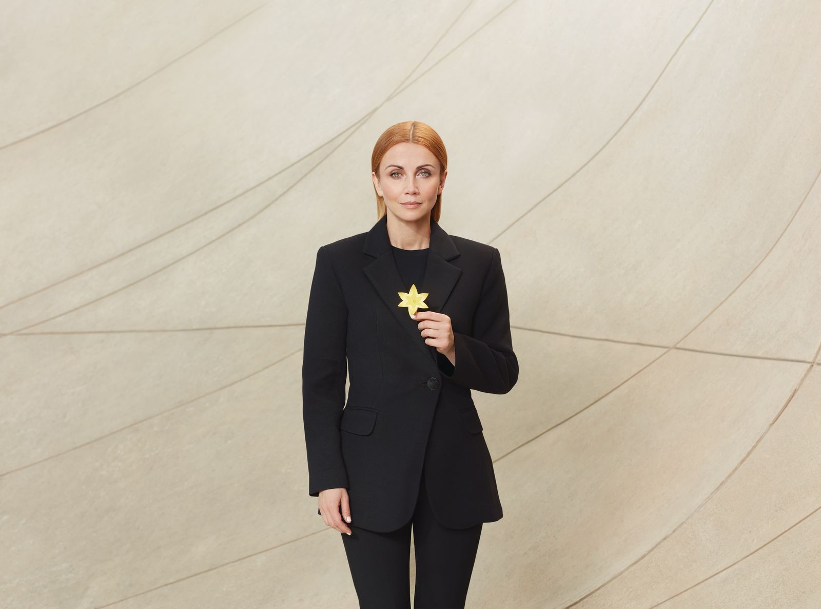 Katarzyna Zielińska w czarnym garniturze trzyma przed sobą w dłoni, na wysokości klatki piersiowej, żółty żonkil, symbol akcji