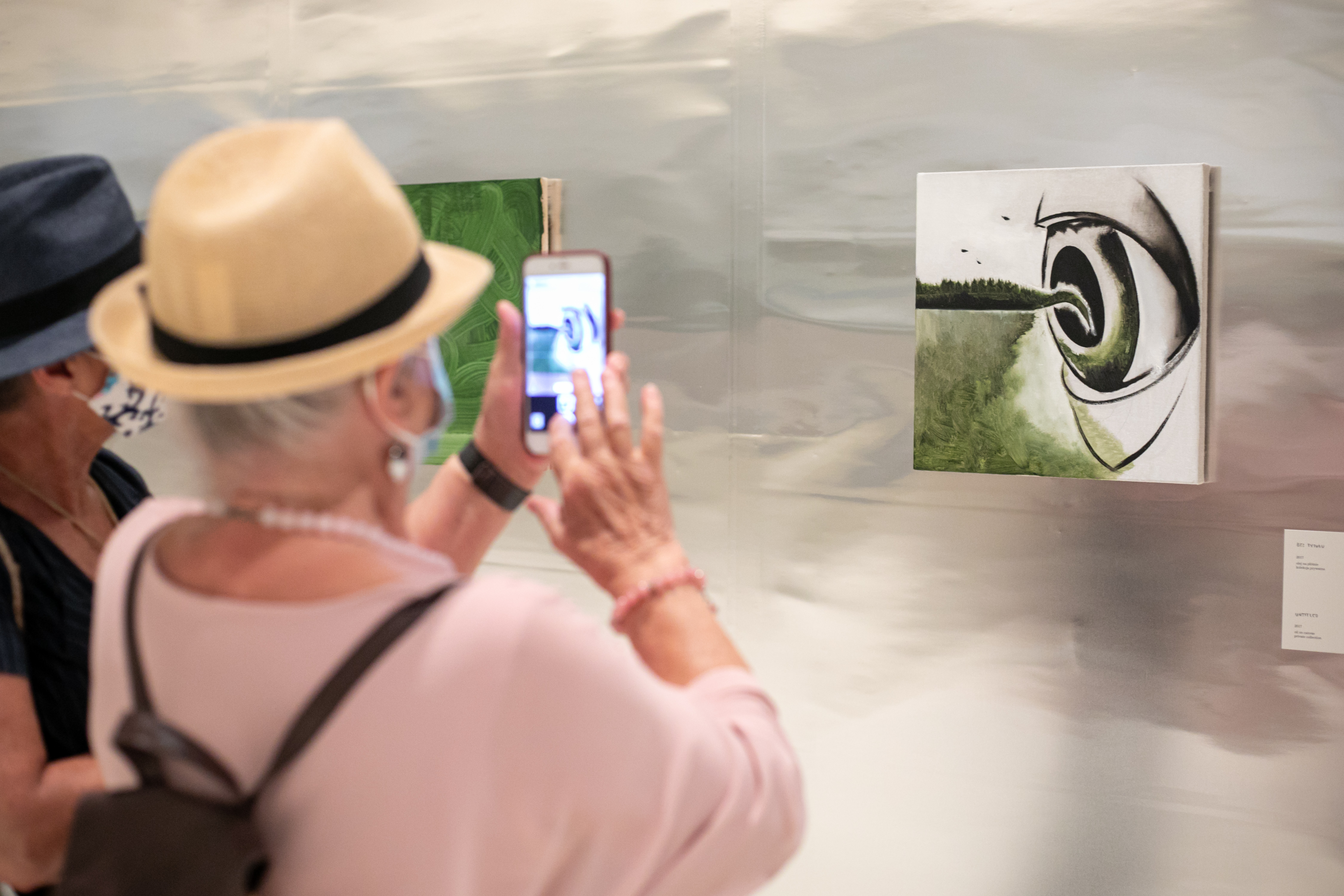 Na obrazie widzimy kobiety robiące zdjęcia jednej obrazom w sali wystawienniczej. 