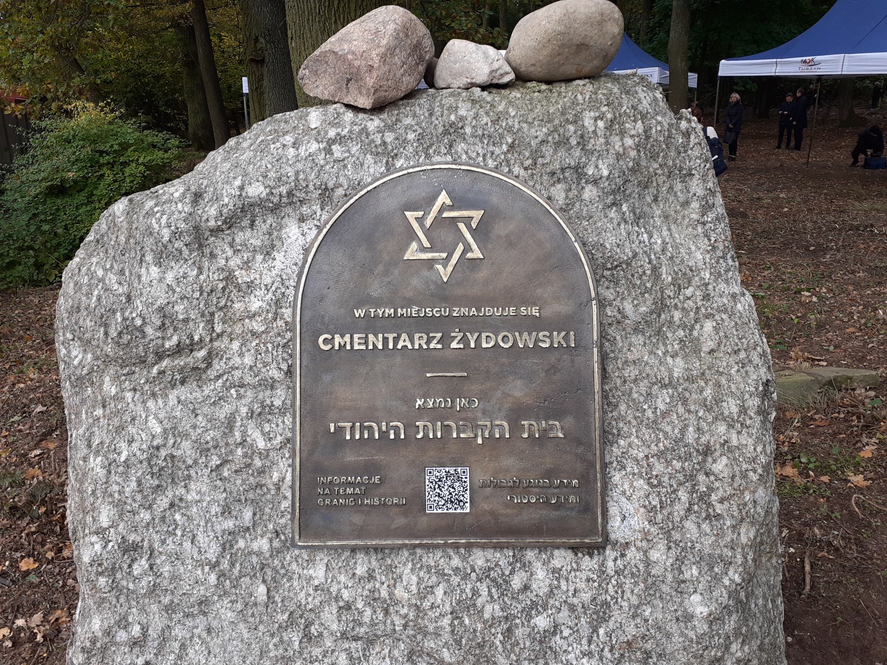 Tablica upamiętniająca cmentarz żydowski w Tuszynie, wmurowana w kamień. Na górze leżą trzy kamyki.