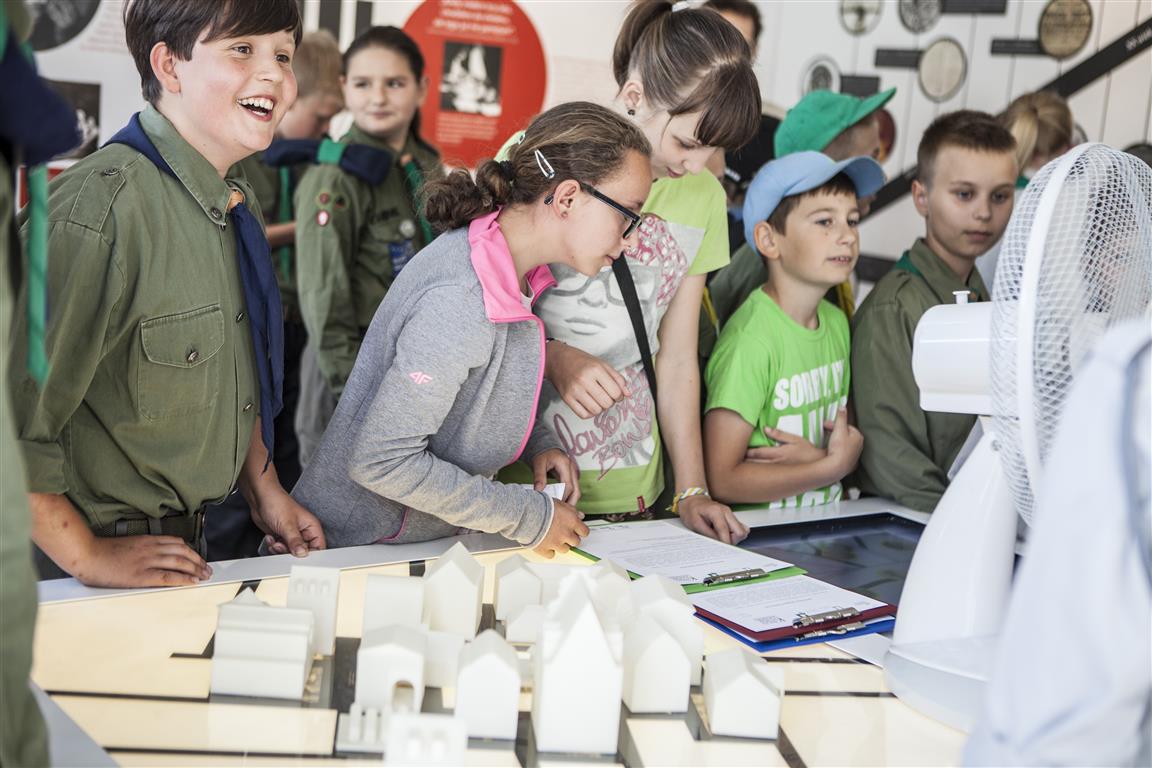 Grupa dzieci i nastolatków zgromadzona wokół makiety na wystawie "Muzeum na kółkach".
