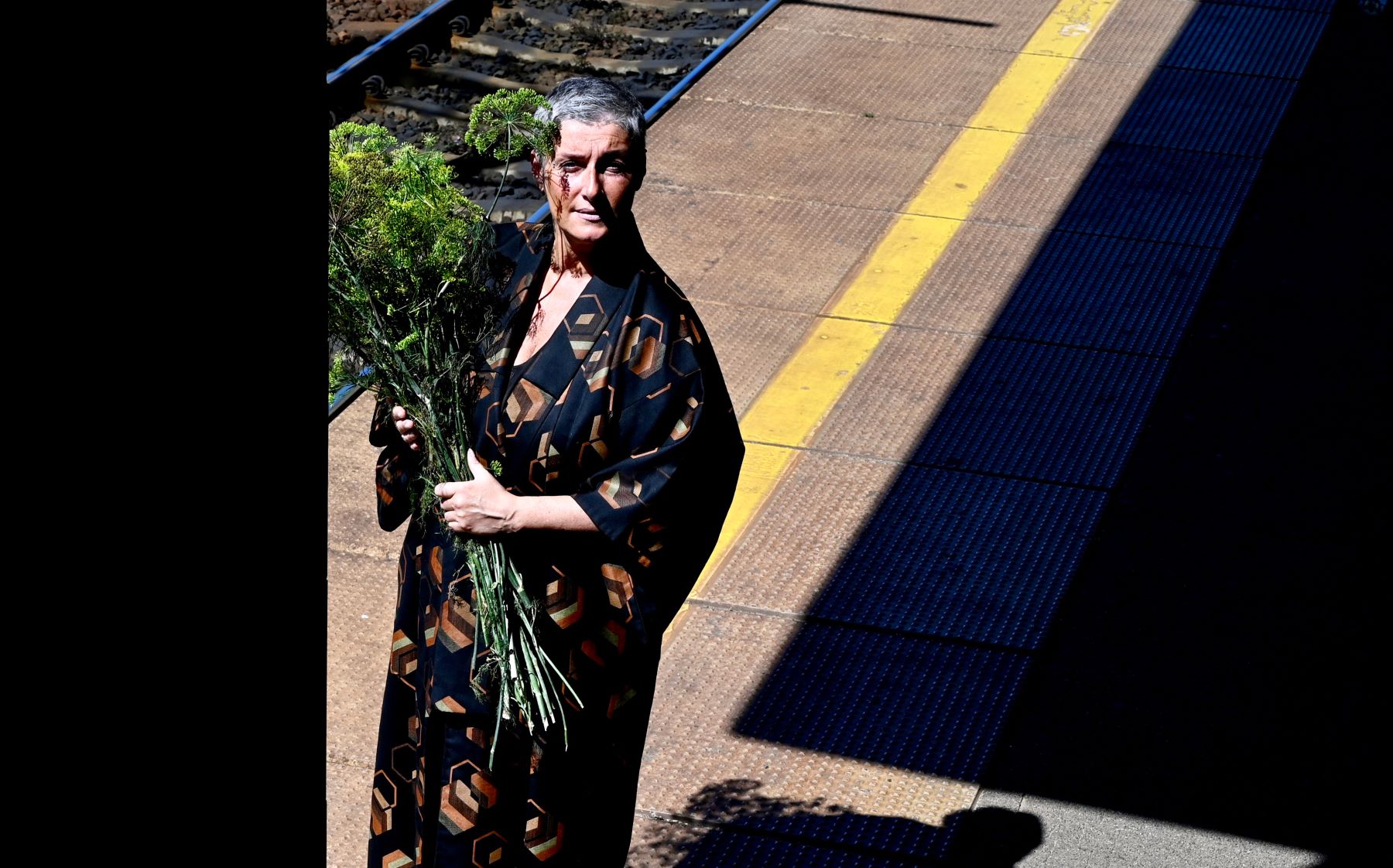 Anna Królikiewicz stoi na peronie dworca. Trzyma zielony koper w dłoniach.
