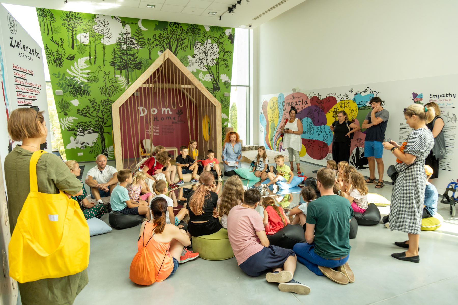 Dzieci i rodzice siedzą na podłodze na wystawie "Elementarz empatii" w Łodzi.