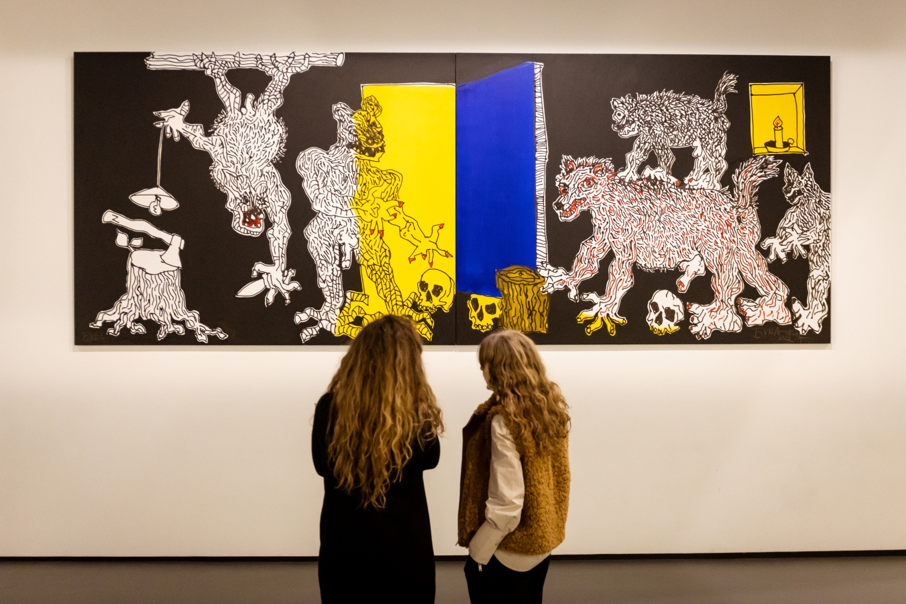 Dwie kobiety stoją przed obrazem Andrzeja Fogtta z serii "Bucza" prezentowanym w Muzeum POLIN.