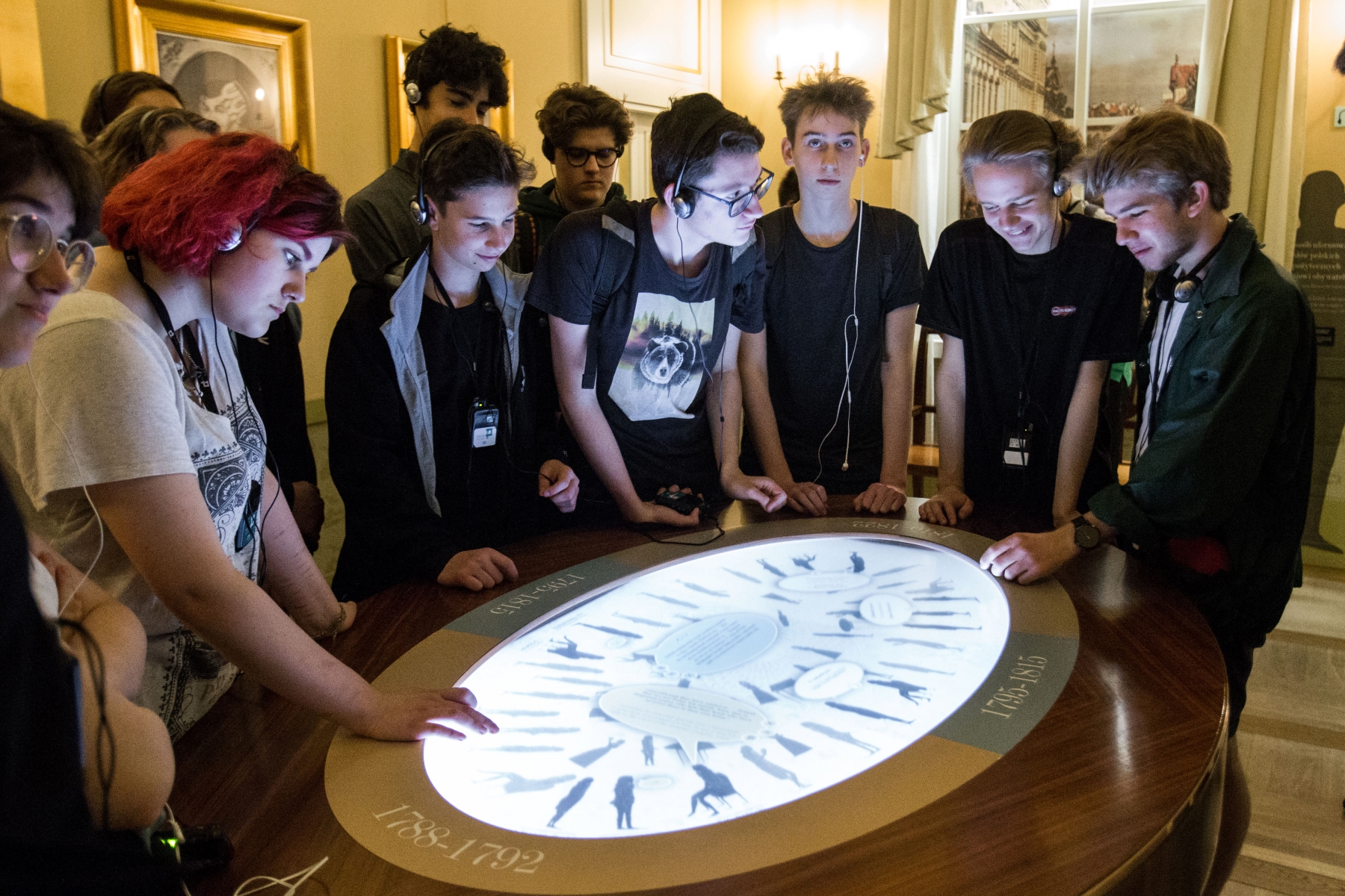 Grupa młodzieży stoi wokół interaktywnego stołu na wystawie stałej w Muzeum POLIN.