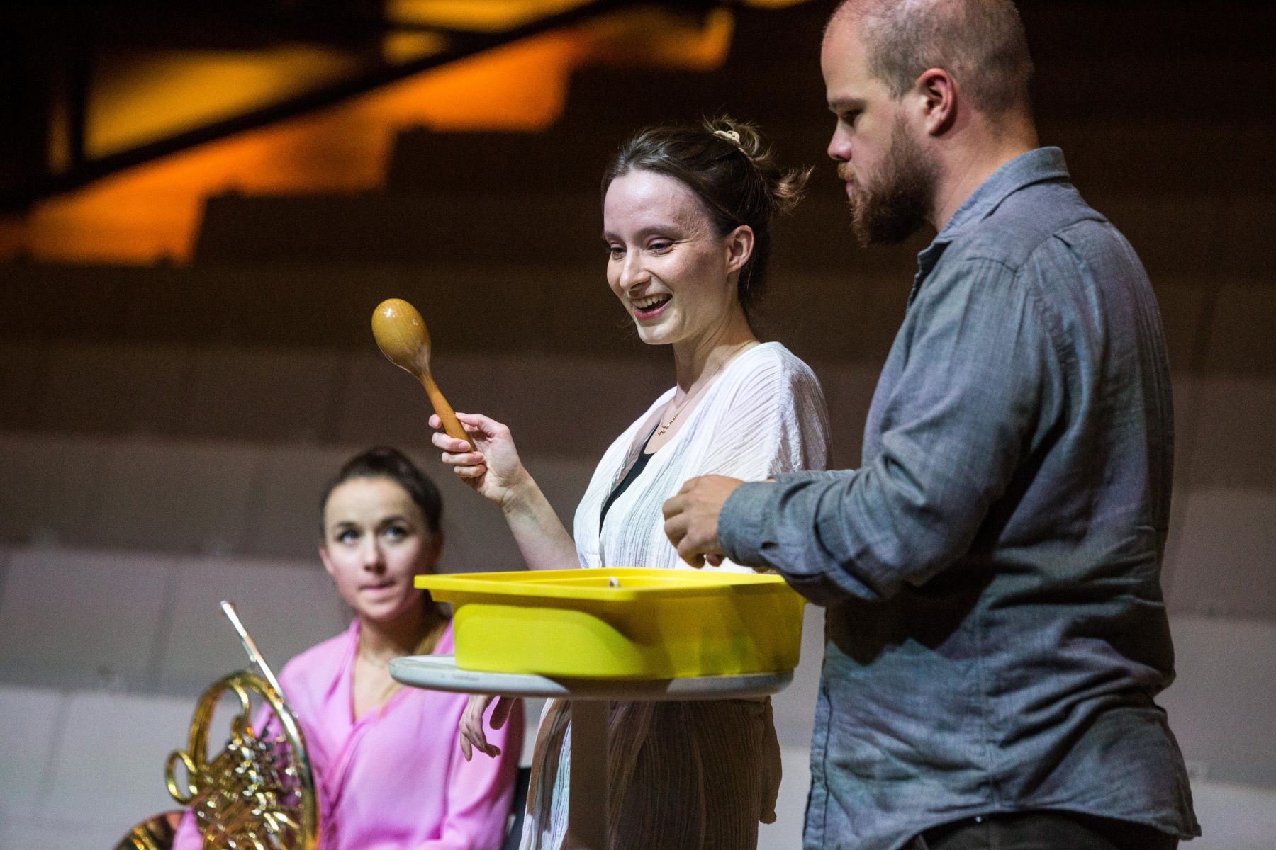 Na scenie w Audytorium Muzeum POLIN: kobieta z instrumentem dętym, Elżbieta Grab z marakasem i Kajetan Prochyra przy żółtym naczyniu.