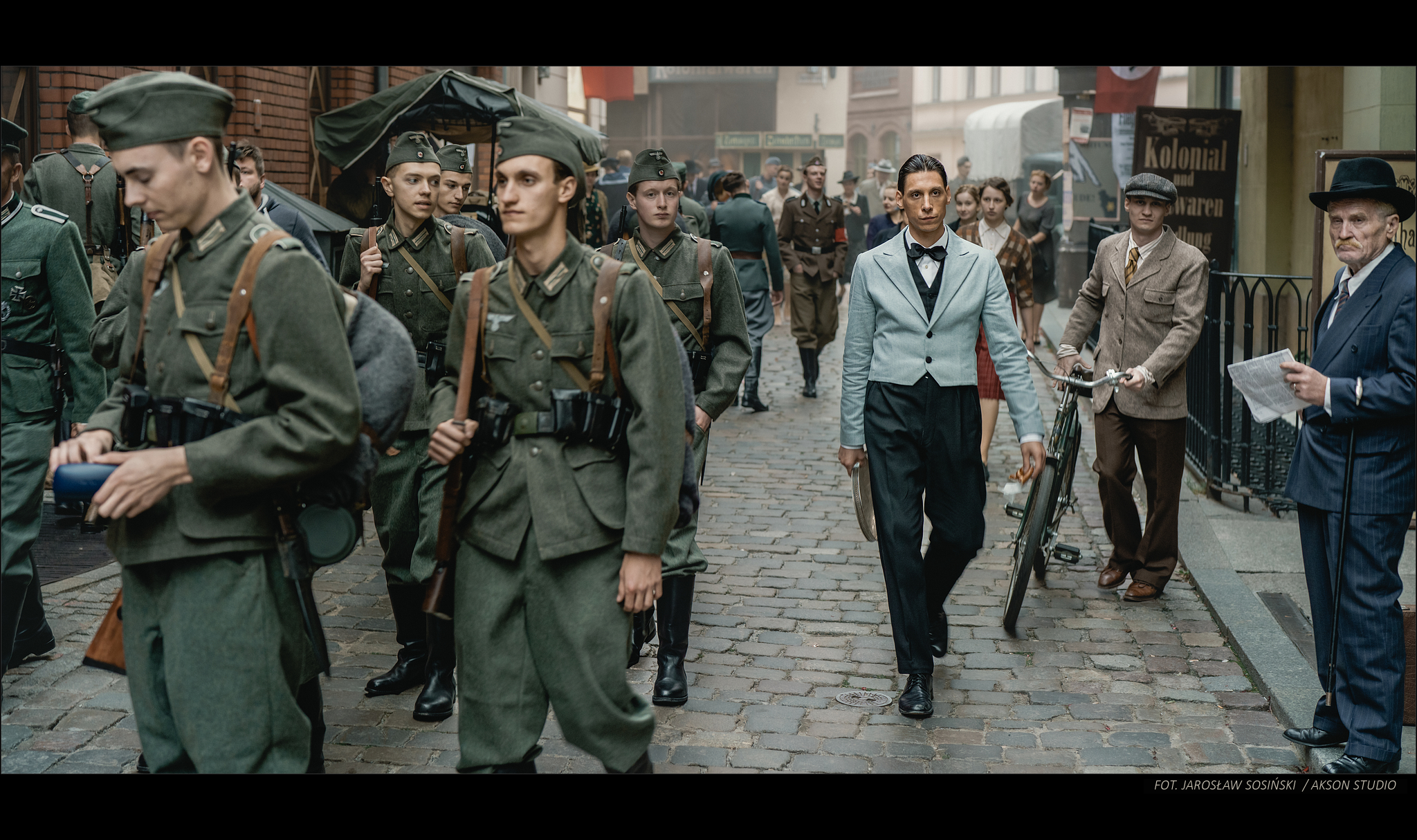 Filip idzie po zatłoczonej ulicy. Obok niego idą niemieccy żołnierze.