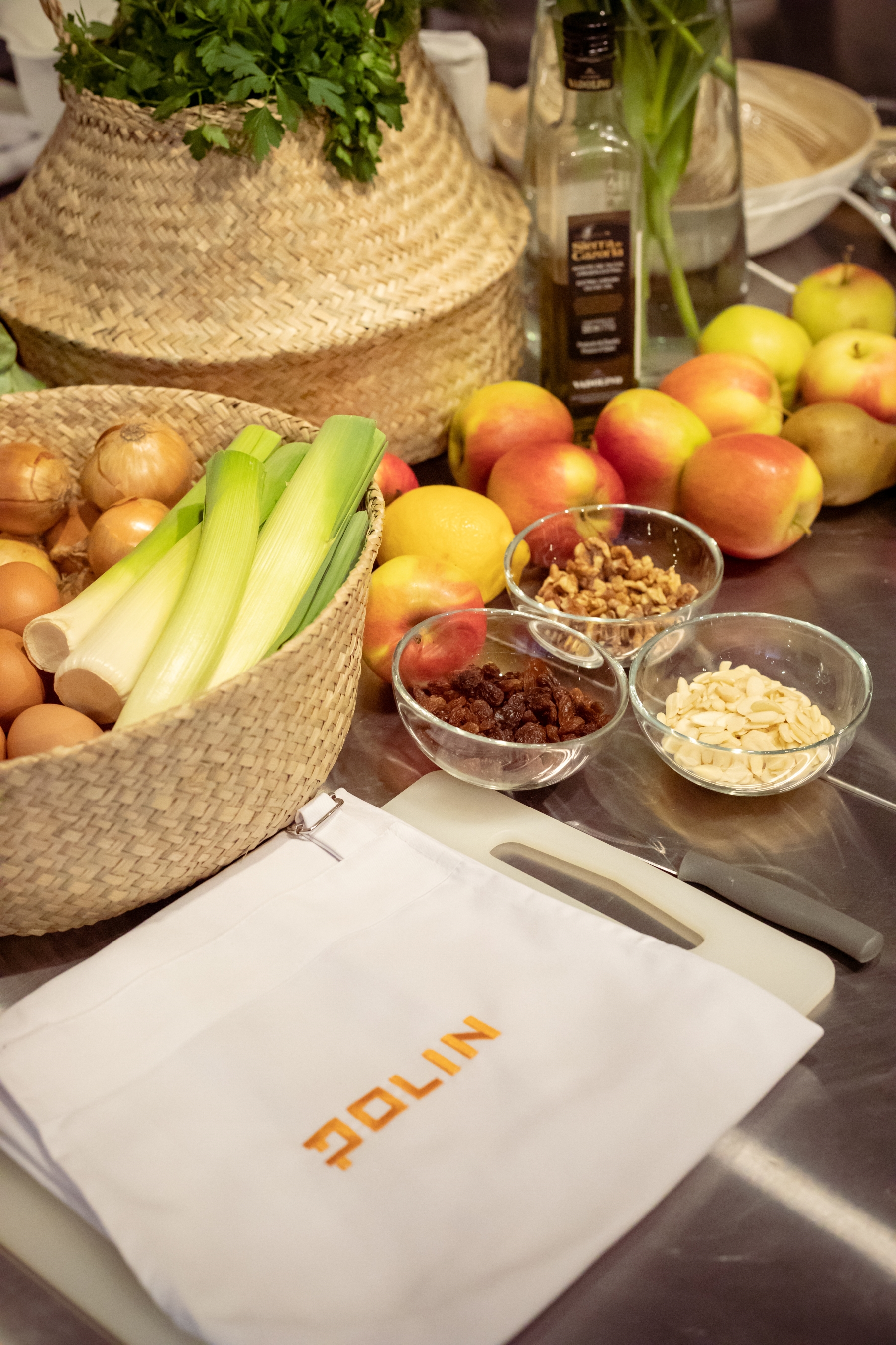 Na stole w Pracowni kulinarnej "U Fani" leżą jabłka i stoją miseczki z orzechami i bakaliami, miska z cebulą i porem, butelka z oliwą, koszyk z natką pietruszki.