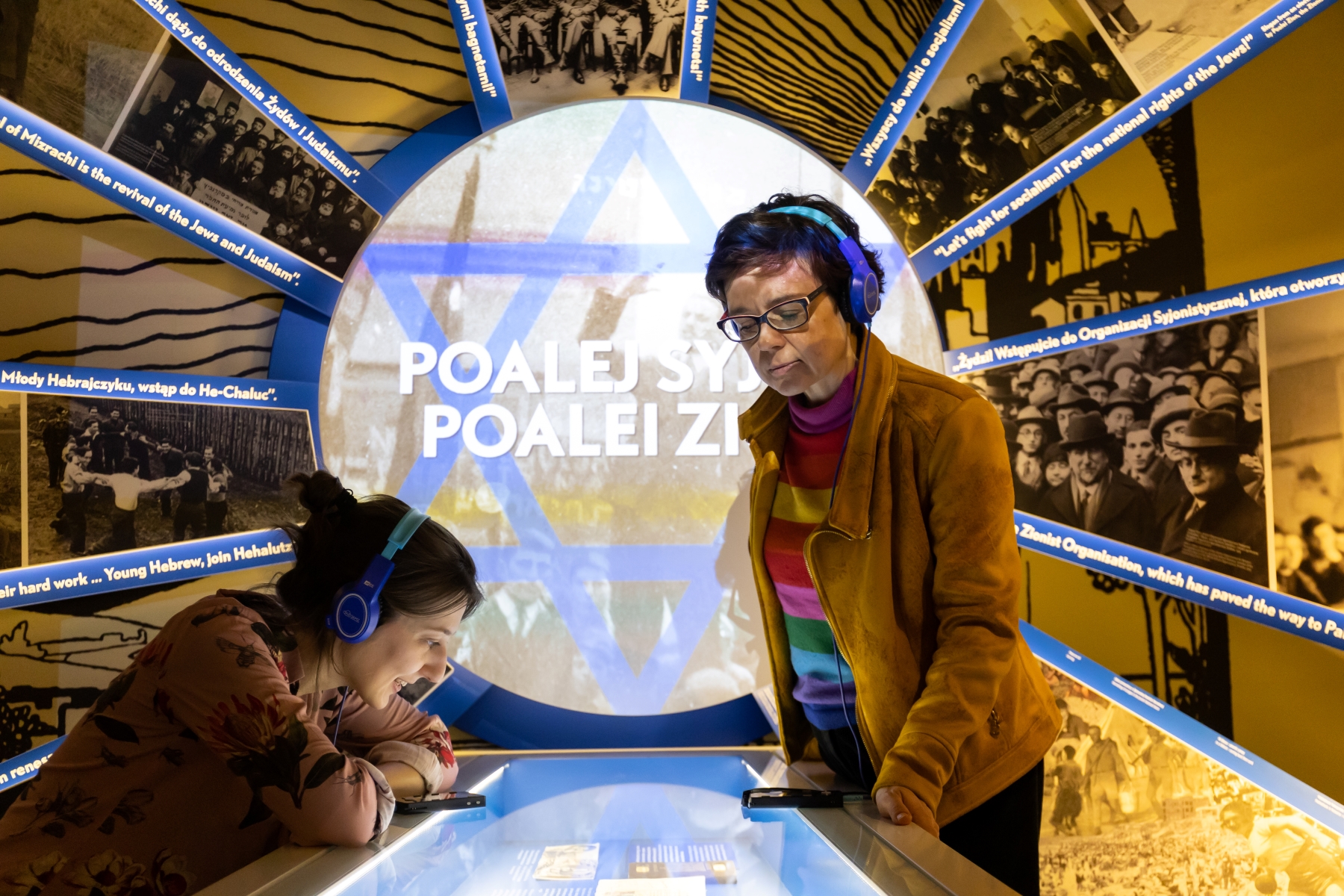Dwie kobiety ze słuchawkami na uszach zwiedzają wystawę stałą w Muzeum POLIN.