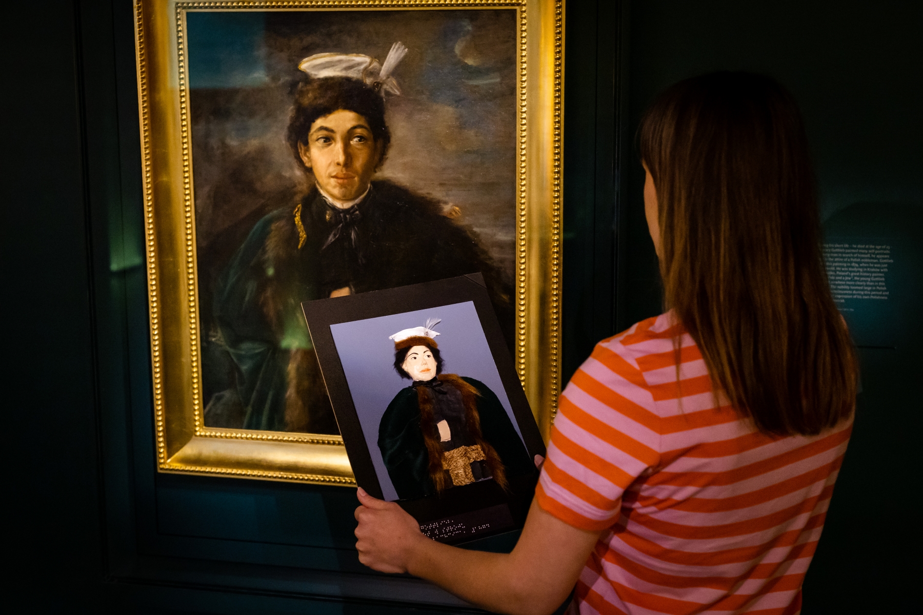 Kobieta stoi przy obrazie Maurycego Gottlieba na wystawie stałej w Muzeum POLIN i trzyma przed sobą tyflografikę tego obrazu.