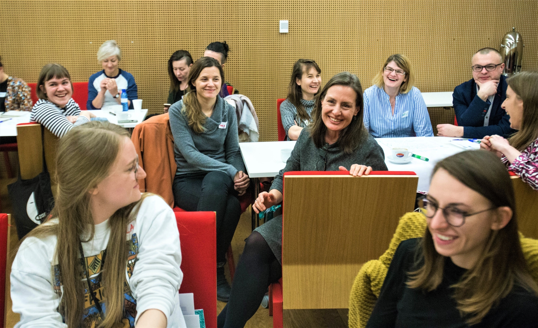 Grupa uśmiechniętych osób, głównie kobiet, siedzi na krzesłach w sali konferencyjnej w Muzeum POLIN.