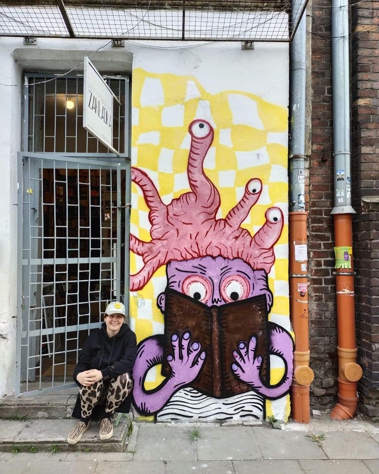 Dorota Cieślik (Miss Dorys( kuca przy muralu przedstawiającym ośmiornicę czytającą książkę.