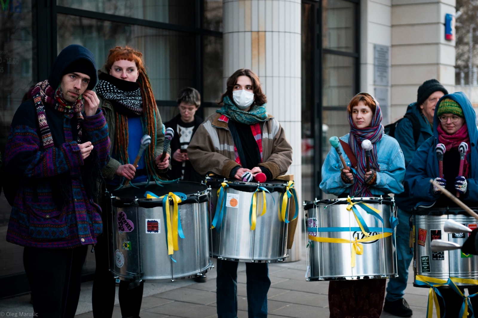 Aktywiści z grupy Samba Warszawski Rumor stoją z bębenkami przy jakimiś budynku w Warszawie.