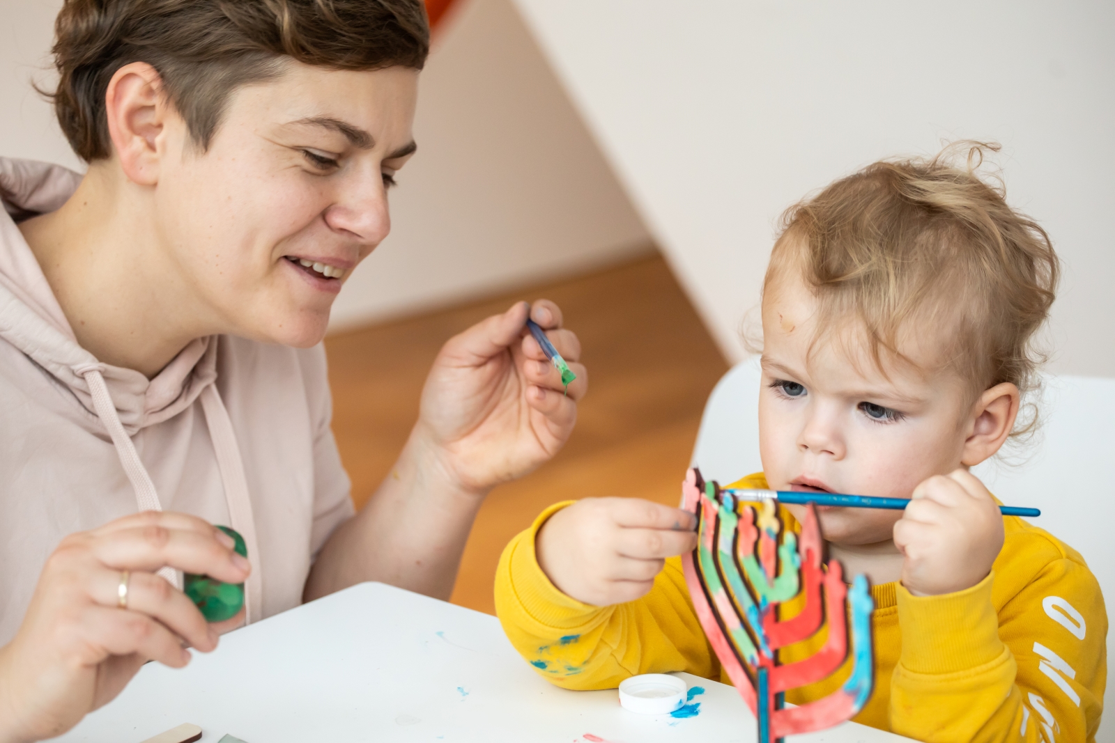 Kobieta i dziecko malują kolorowymi farbami model drewnianego świecznika.