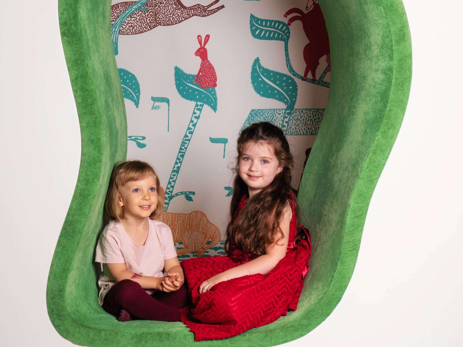 Dwie dziewczynki siedzą w kolorowej pluszowej wnęce w Miejscu edukacji rodzinnej "U króla Maciusia".