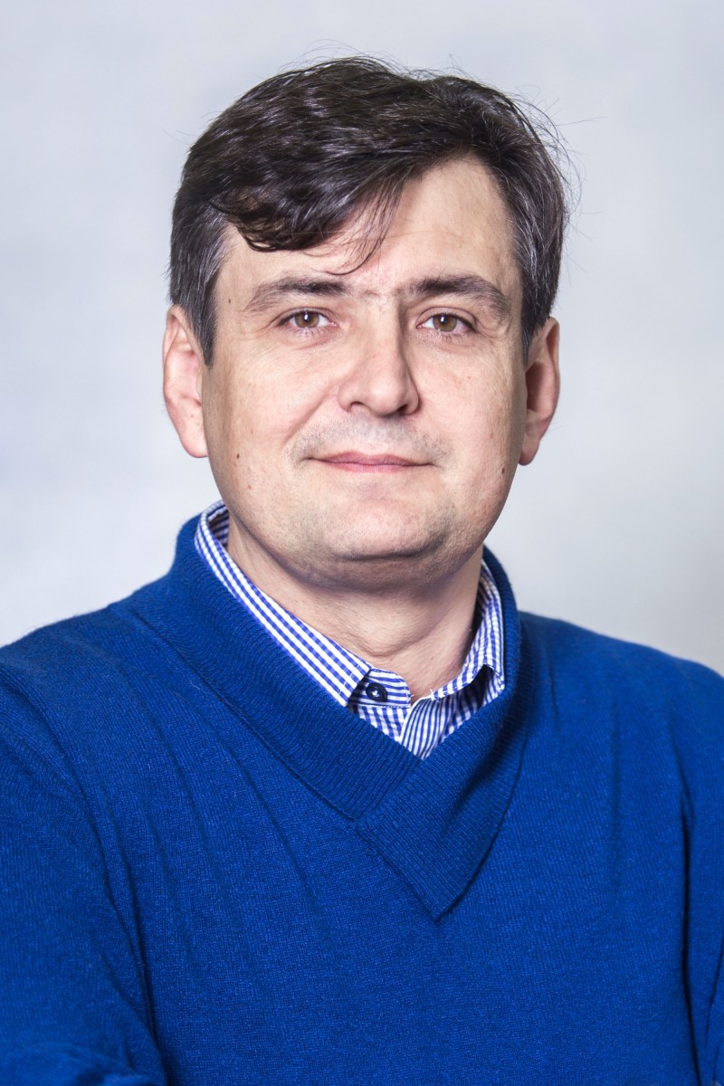 Zdjęcie portretowe. Mirosław Skrzypczyk - wyróżnienie w konkursie Nagroda POLIN 2016. Szatyn w niebieskim swetrze i wzorzystej koszuli.