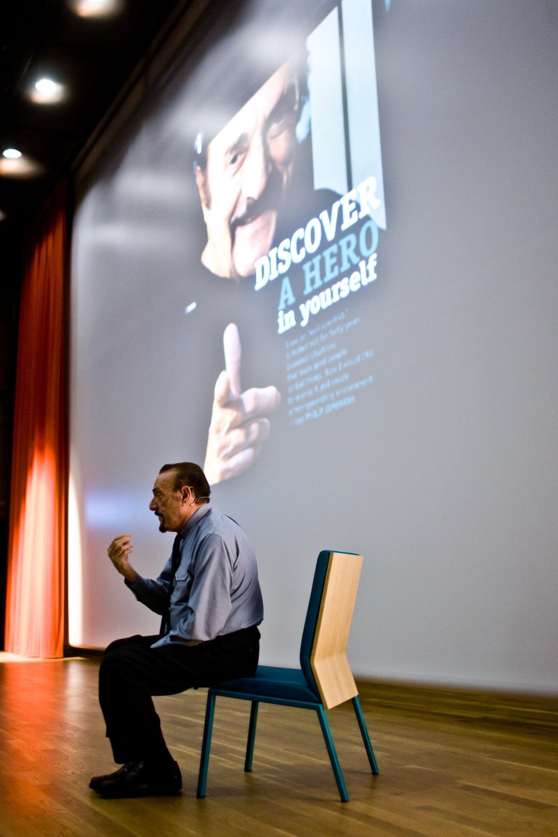 Philip Zimbardo siedzi na krześle podczas wykładu.