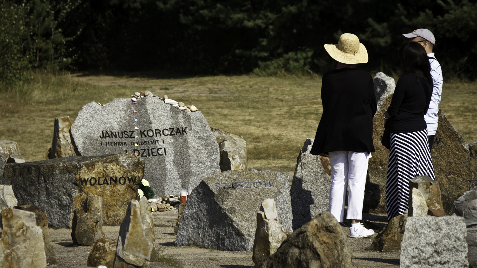 Trzy osoby stoją przy kamieniu upamiętniającym Janusza Korczaka.