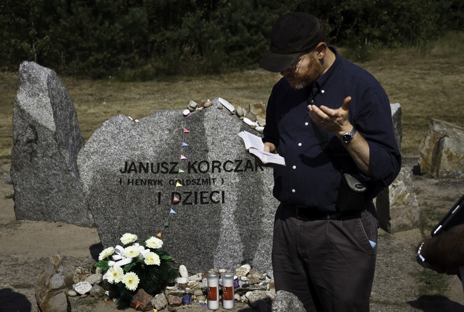 Mężczyzna stoi przy tablicy upamiętniającej Janusza Korczaka i odmawia modlitwę.