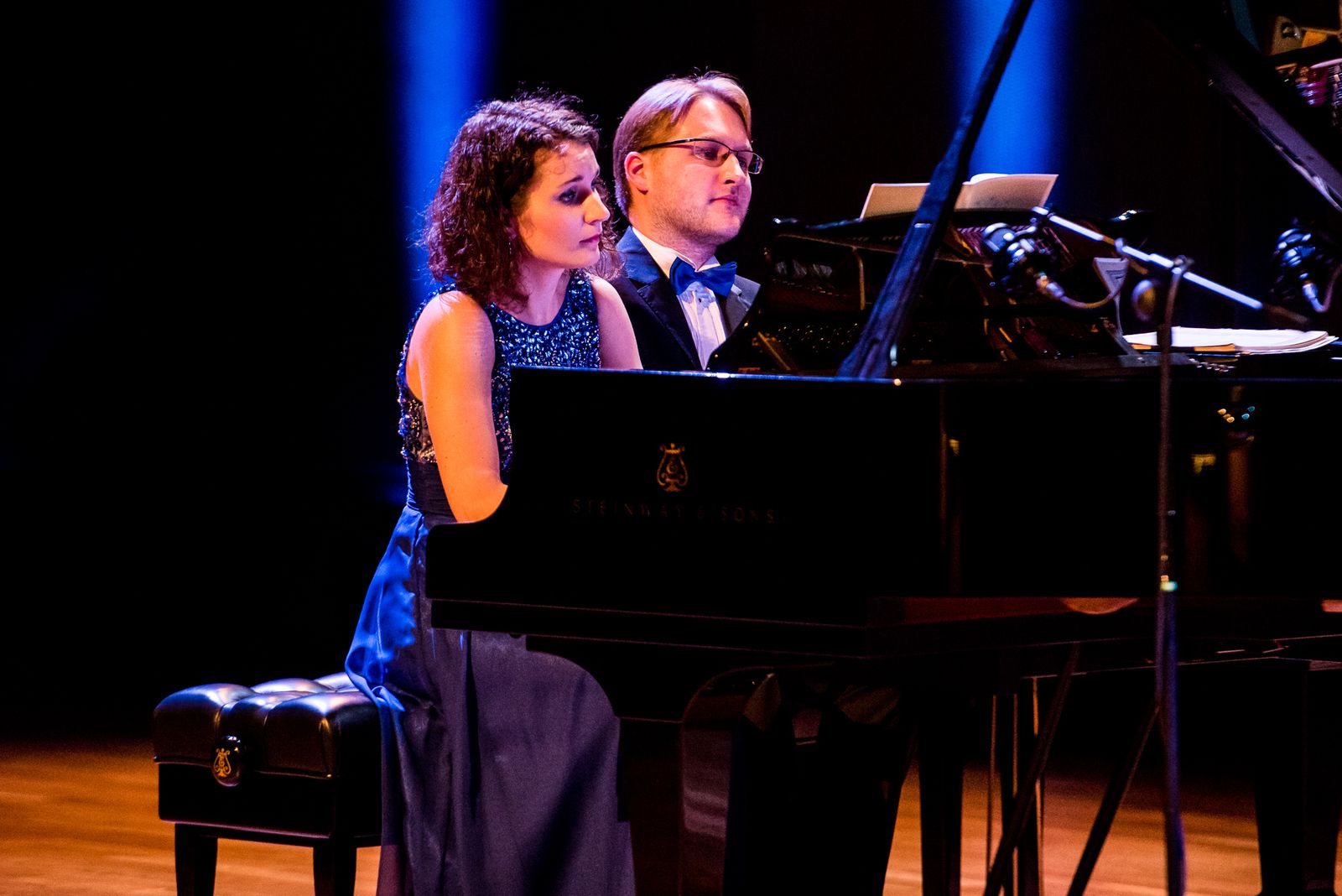 Przy fortepianie ustawionym na scenie dwójka pianistów: kobieta i mężczyzna
