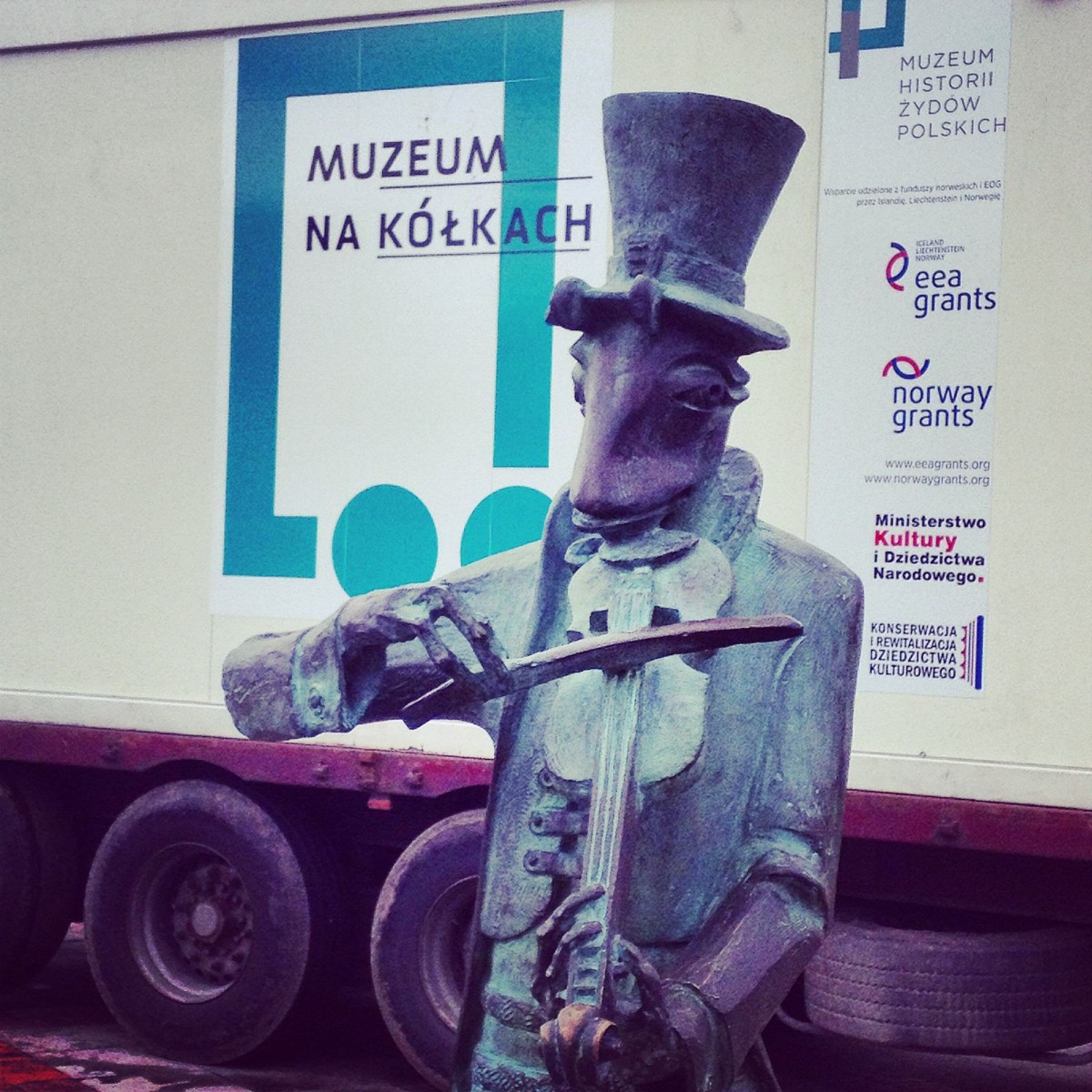 Chrząszcz ze Szczebrzeszyna (posąg) gra na skrzypcach przed wagonikiem z napisem Muzeum na kółkach.