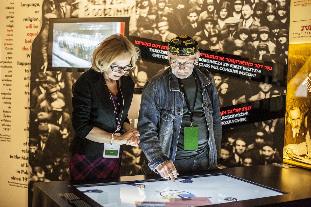 Dwoje zwiedzających przy ekranie multimedialnym na wystawie stałej w POLIN.