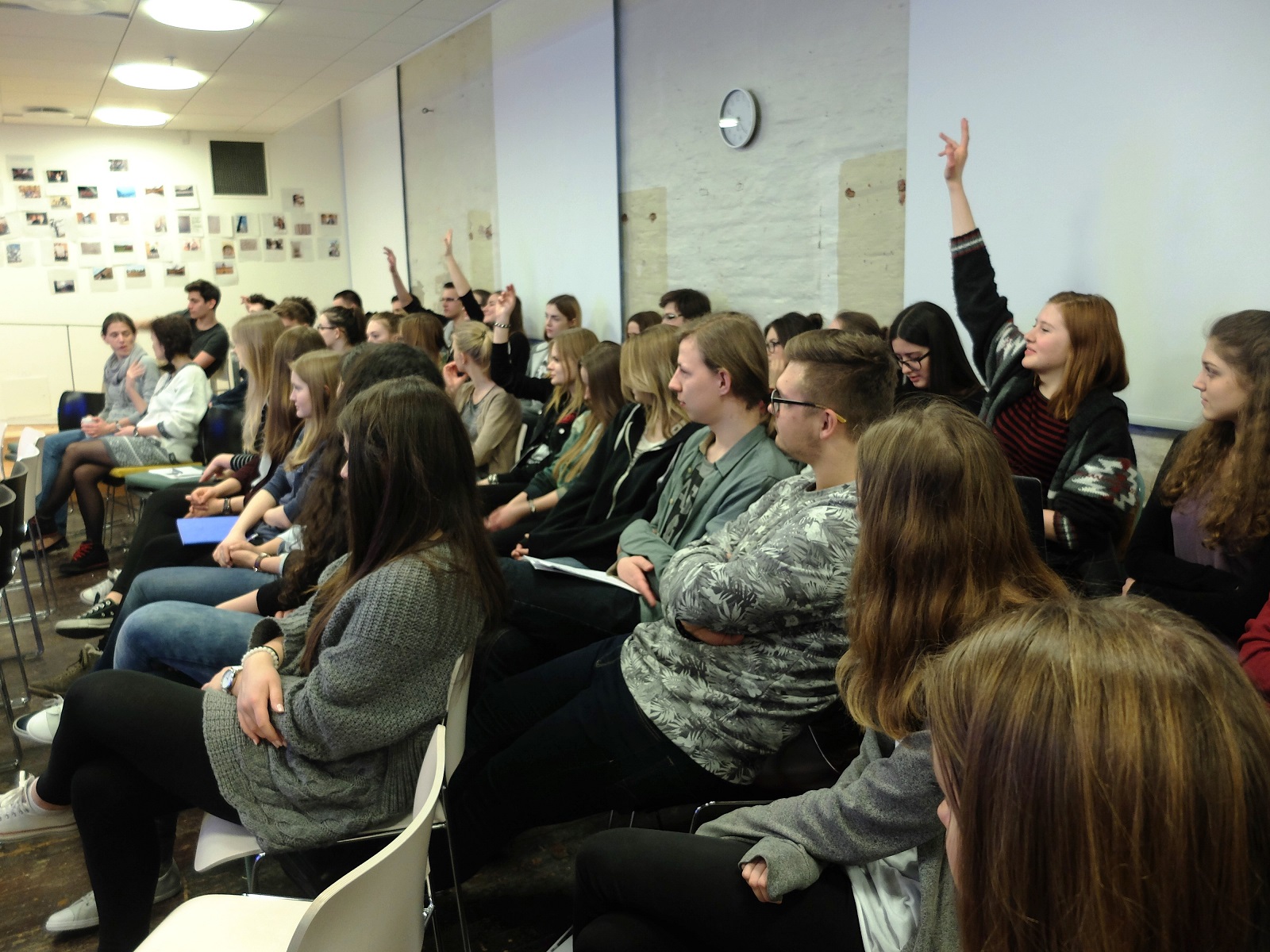 Uczestnicy w konferencji w sali wykładowej - jedna osoba podnosi rękę do góry.
