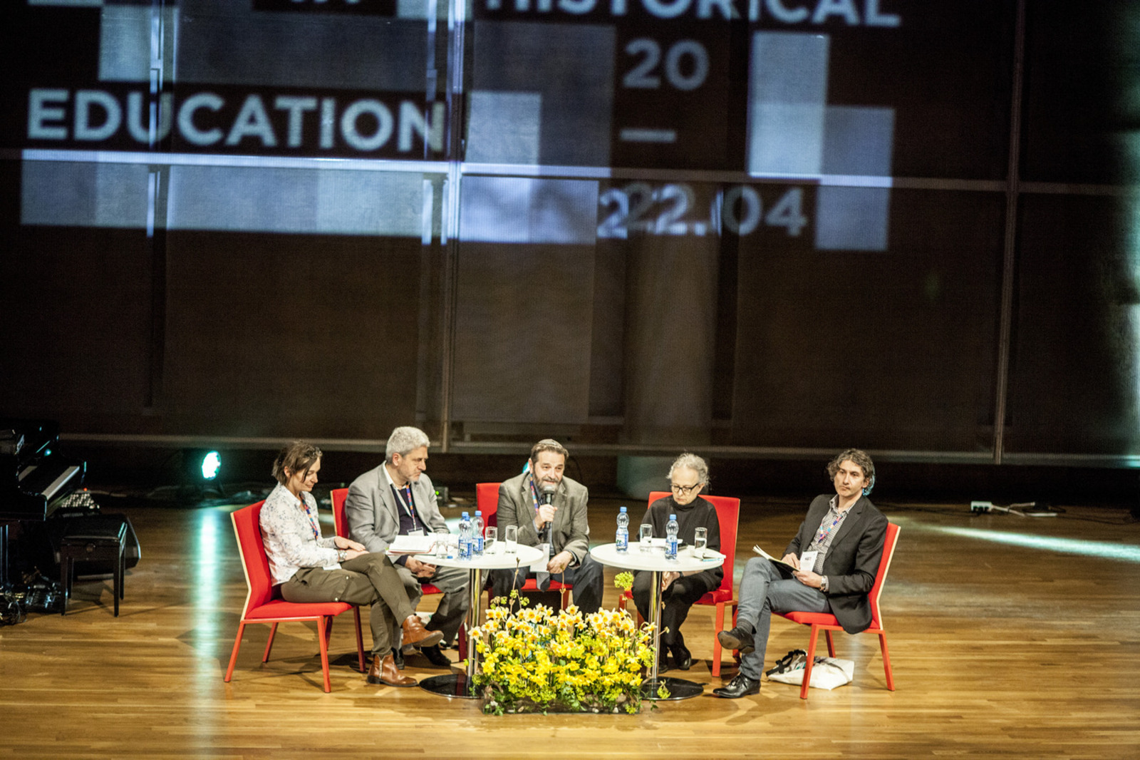 Pięć osób siedzi na krzesłach na scenie podczas konferencji.