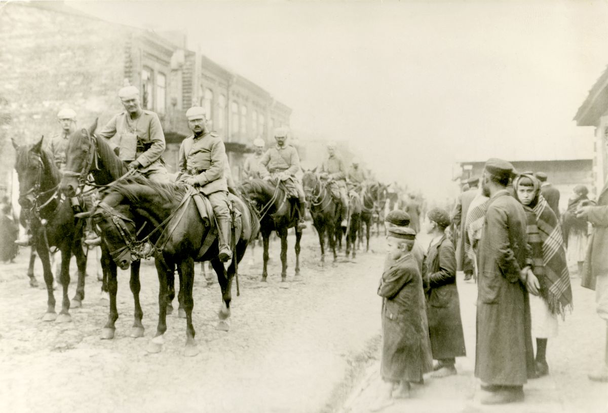Fotografia archiwalna. Legioniści na koniach. Przyglądają im się ludzie stojący na ulicy.