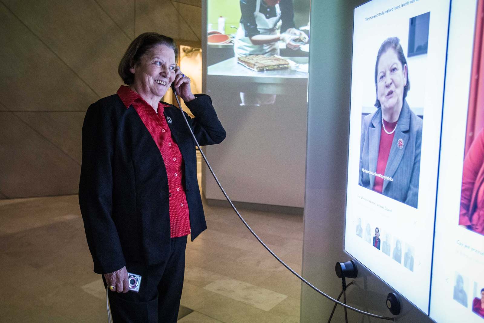 Muzeum POLIN - kobieta słucha nagrania przez słuchawkę. Na ekranie wyświetla się jej podobizna.
