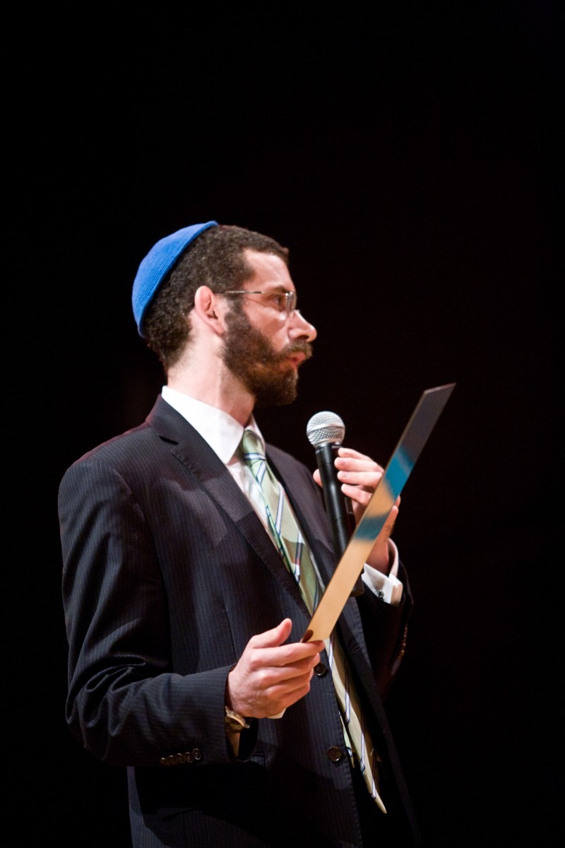 Żyd w mycce stoi z mikrofonem.