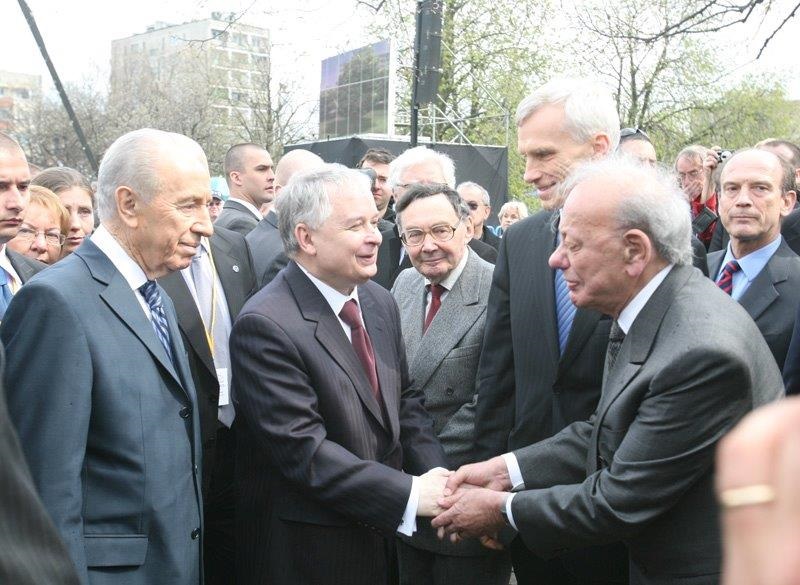 Lech Kaczyński wita się z innym mężczyzną poprzez uścisk dłoni.