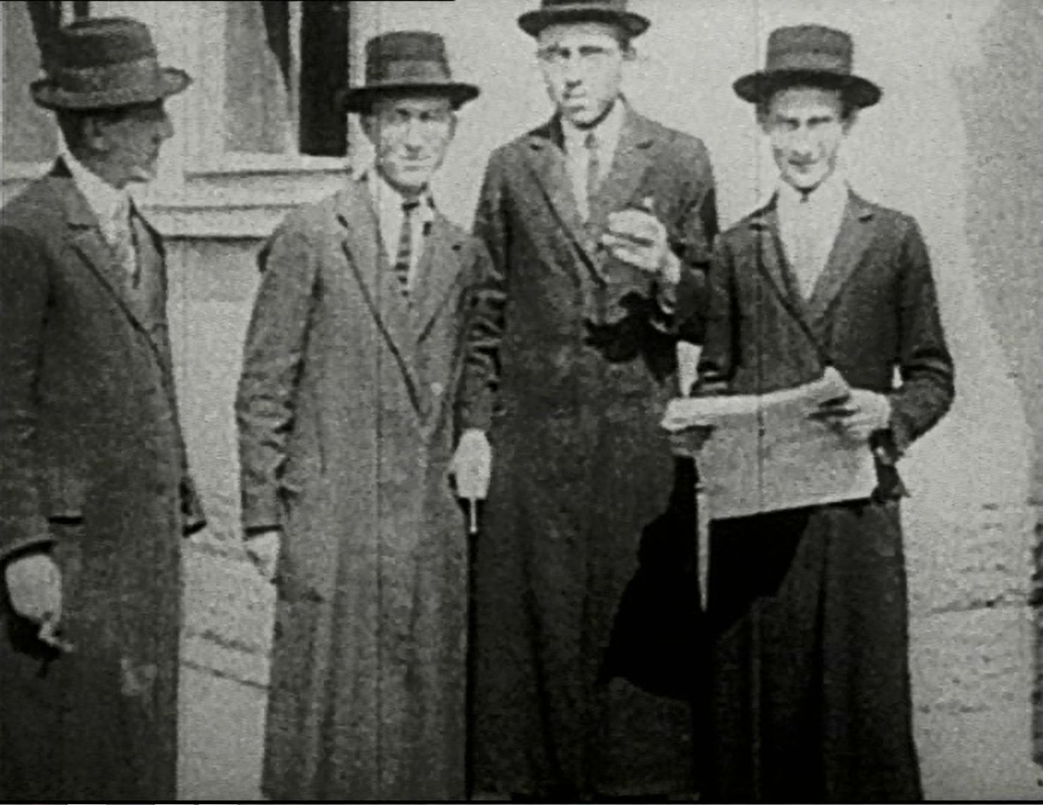 Zdjęcie archiwalne przedstawia czterech Żydów w kapeluszach i długich płaszczach.