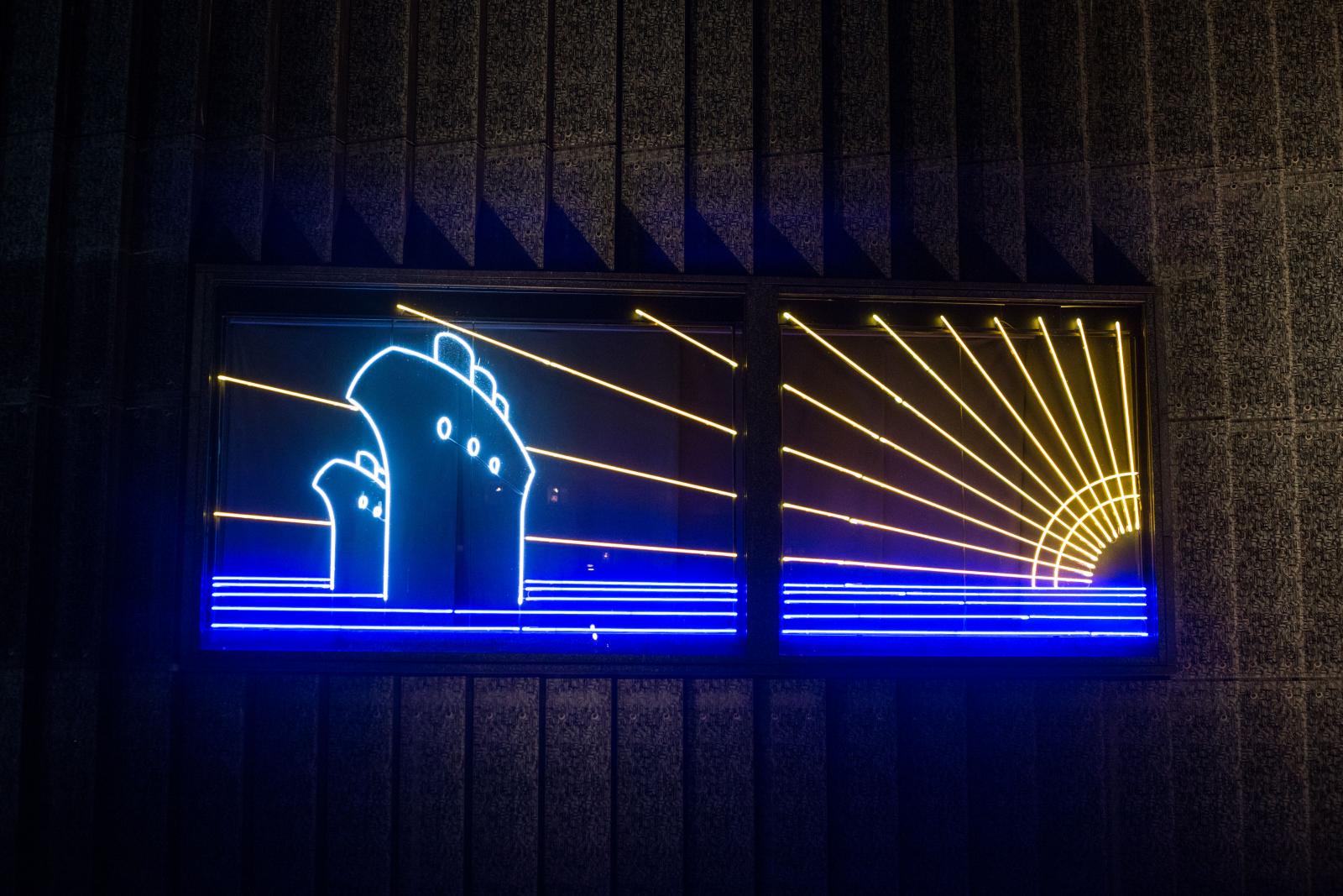 Wystawa czasowa "Gdynia - Tel Awiw" w Muzeum POLIN. Na zdjęciu neon zaprojektowany przez Maurycego Gomulickiego, który przedstawia dwa transatlantyki na morzu, oświetlone promieniami zachodzącego słońca. Neon utrzymany w kolorach białym, niebieskim i żółtym