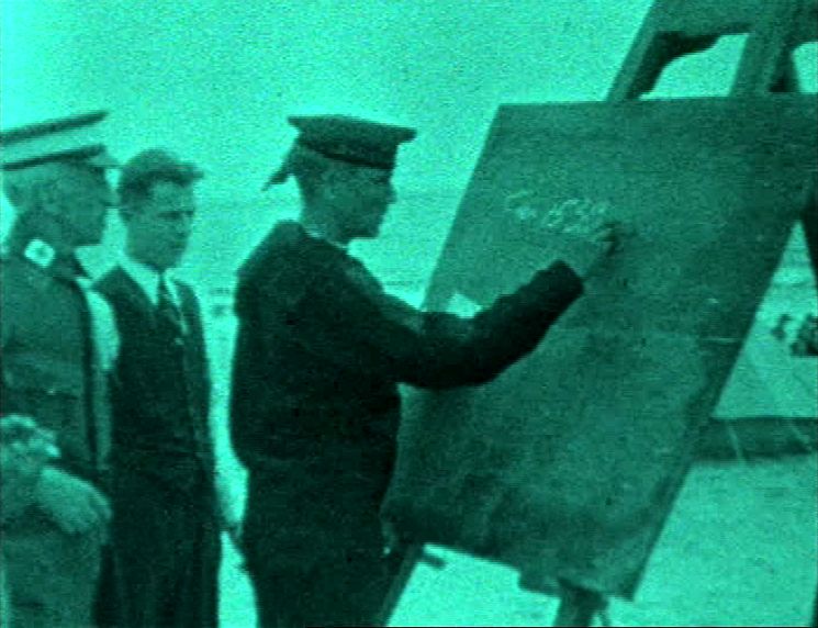 Zdjęcie w zielonym odcieniu. Mężczyzna w mundurze pisze na tablicy.