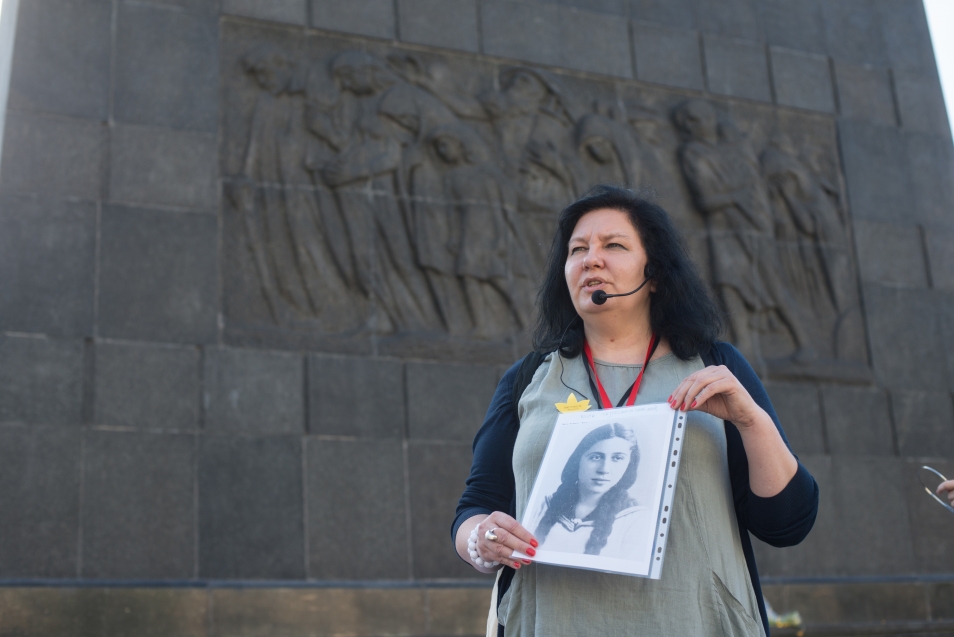 Przewodniczka - Katarzyna Jakubowicz - prezentuje zdjęcie jednej z bohaterek spaceru. W tle pomnik Bohaterów Getta przed Muzeum POLIN w Warszawie
