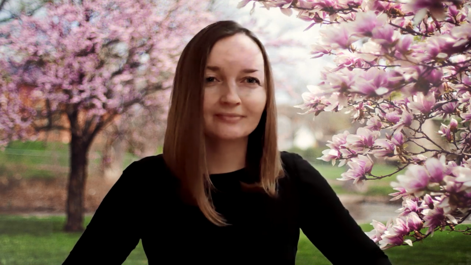 Na zdjęciu kobieta w czarnej bluzce, w tle magnolie - kwitną różowymi kwiatami