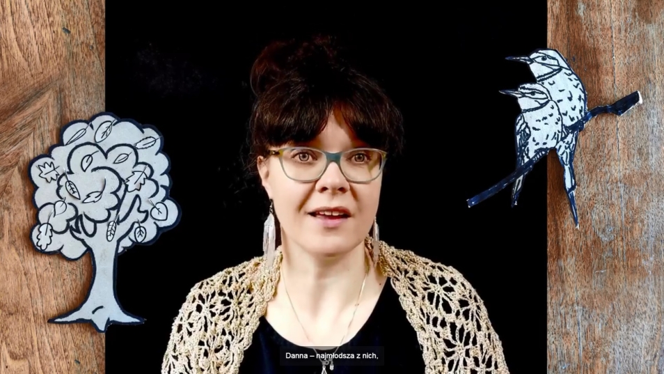 Na zdjęciu kobieta. Wokół niej po lewej grafika drzewa, po prawej ptaki, które siedzą na gałęzi