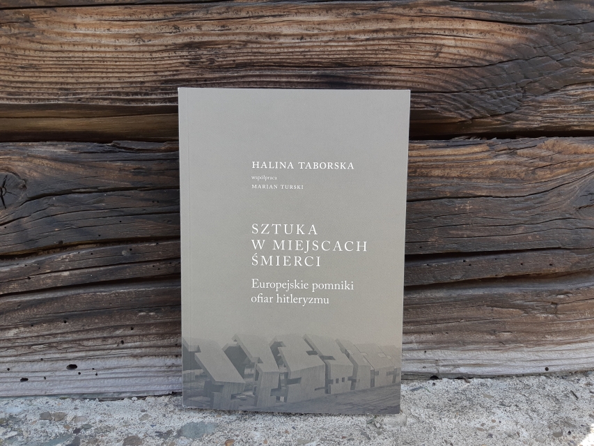 Okładka książki Halina Taborska (współpraca Marian Turski) "Sztuka w miejscach śmierci. Europejskie pomniki ofiar hitleryzmu". Książka oparta o ścianę ze starych drewnianych belek
