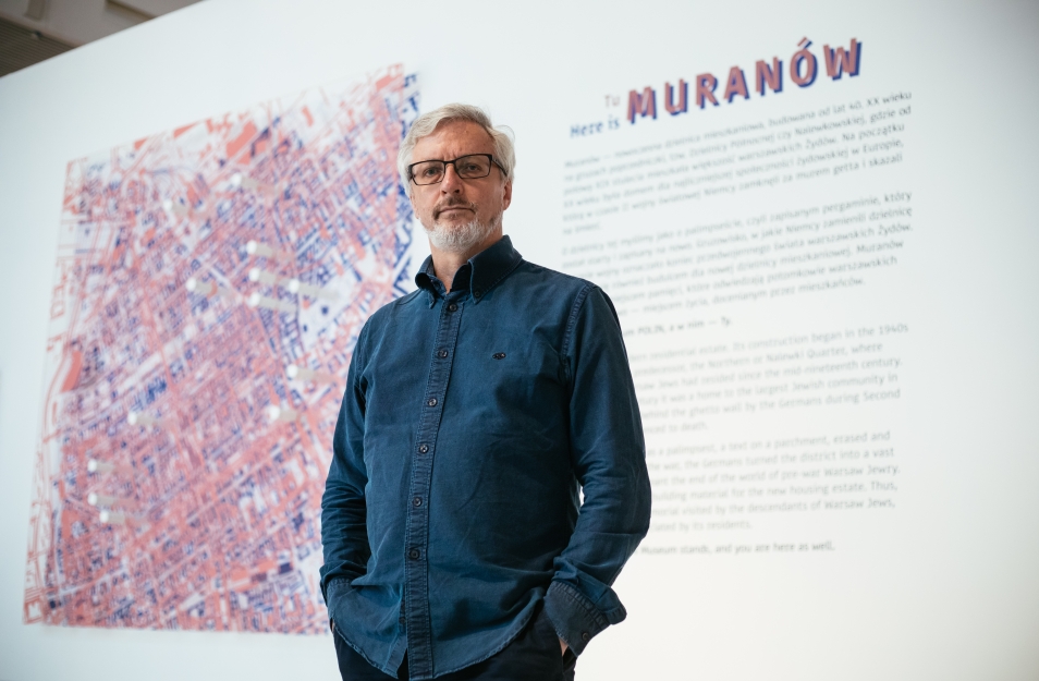 Przed planszą któa otwiera wystawę Tu Muranów stoi mężczyzna - Jacek Leociak. Na planszy opis wystawy oraz mapa Muranowa