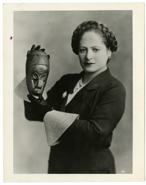 Elegancko ubrana kobieta - Helena Rubinstein - trzyma w dłoniach maskę z drewna Afrykańską