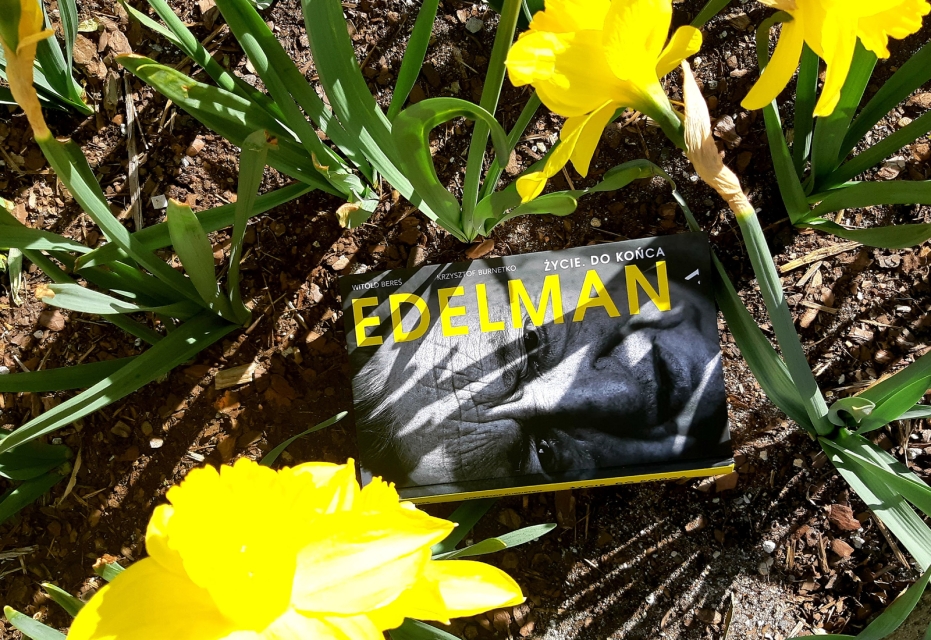 Książka "Marek Edelman - biografia" leży na trawniku, między kwitnącymi żółtymi żonkilami