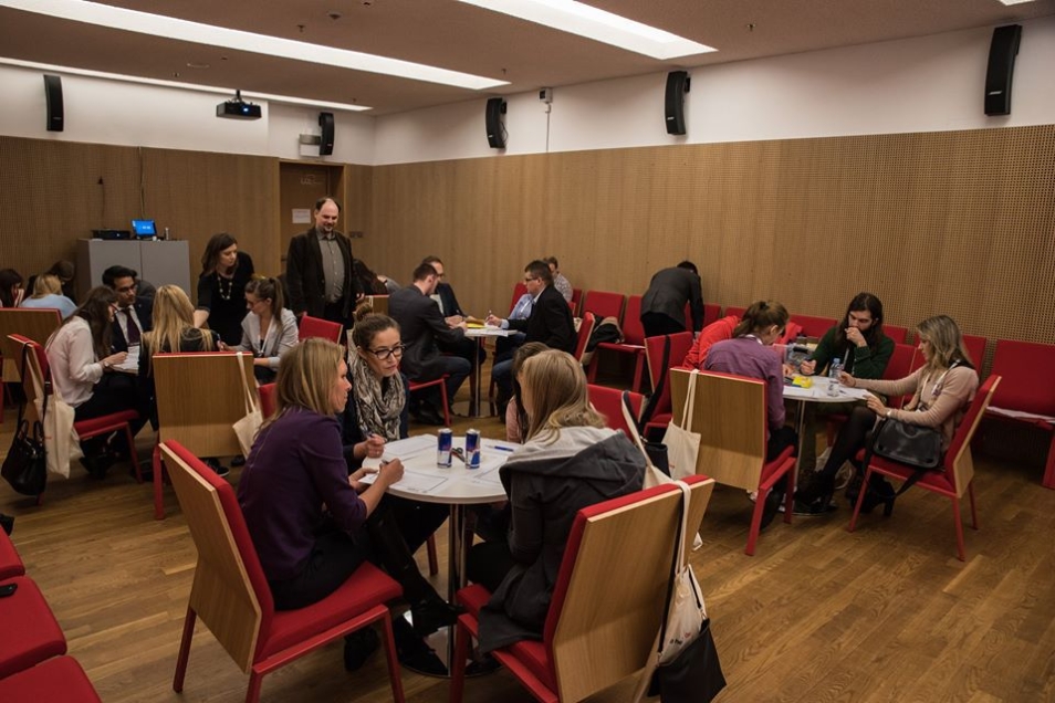 Sala konferencyjna B - ustawienie krzeseł wokół stołów. Na krzesłach siedzą uczestnicy wydarzenia