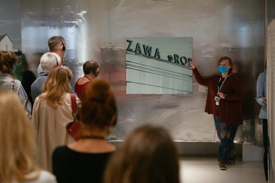 Na obrazie widzimy grupę osób w trakcie odprowadzania z przewodnikiem po wystawie. 