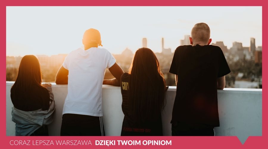 Cztery osoby stoją tyłem, opierają się o betonową balustradę i patrzą na miasto w oddali