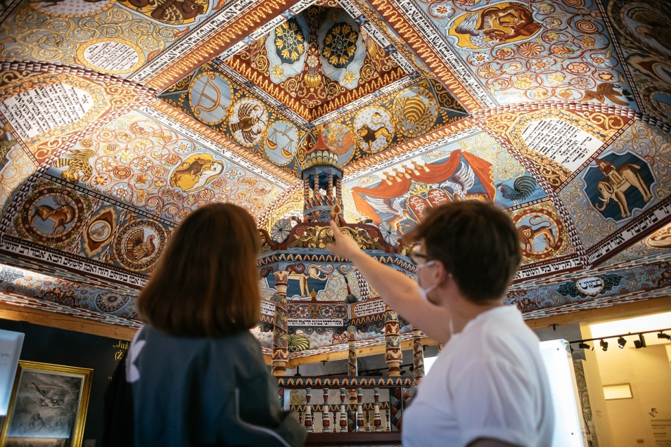 Na obrazie widzimy wnętrze muzeum, w którym grupka osób przygląda się jednemu z eksponatów.. 