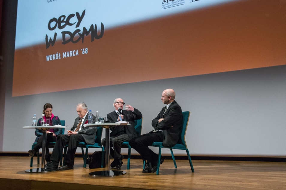 Na scenie na czterech krzesłach siedzą osoby, które biorą udział w dyskusji