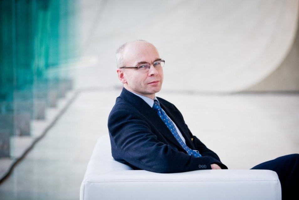 Dariusz Stola. Łysy mężczyzna w okularach i garniturze siedzi na kanapie znajdującej się we wnętrzu Muzeum POLIN.